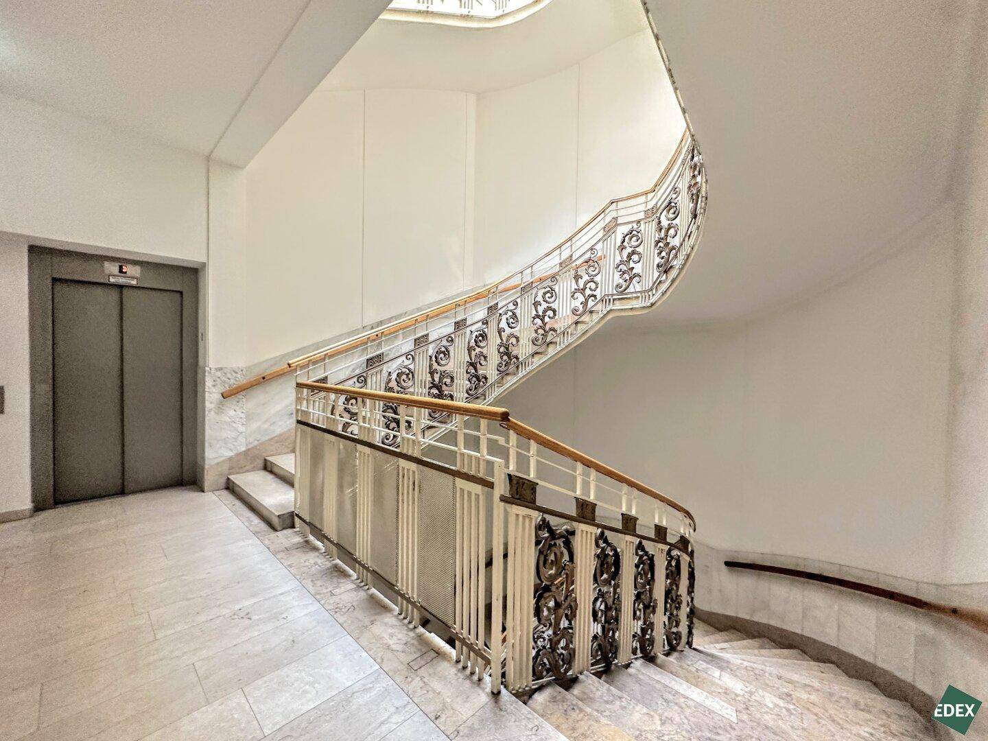 Elegantes Treppenhaus mit kunstvollen Geländern und Marmorstufen, inklusive modernem Aufzug.