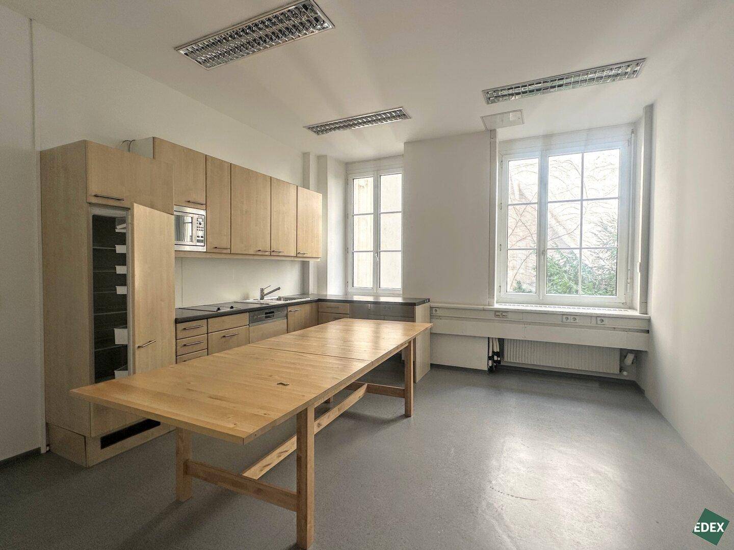Funktionale Teeküche mit Holzschränken, Spüle und einem großen Holztisch, ideal für Pausen.