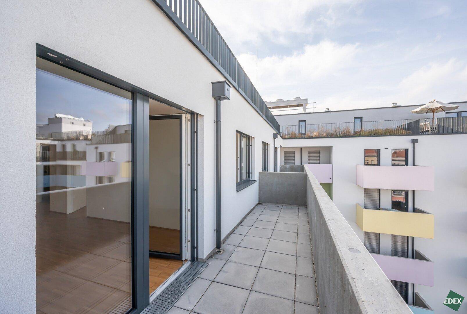 Langer Balkon mit Fliesenboden und Blick auf die Dächer der Stadt und weitere Balkone.