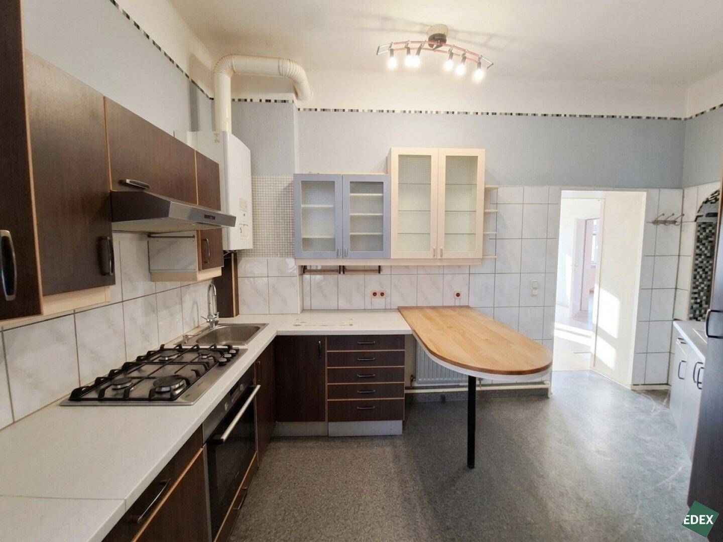 Funktionale Küche mit Gasherd, Backofen, Spüle und integriertem Esstisch in älterem Zustand.