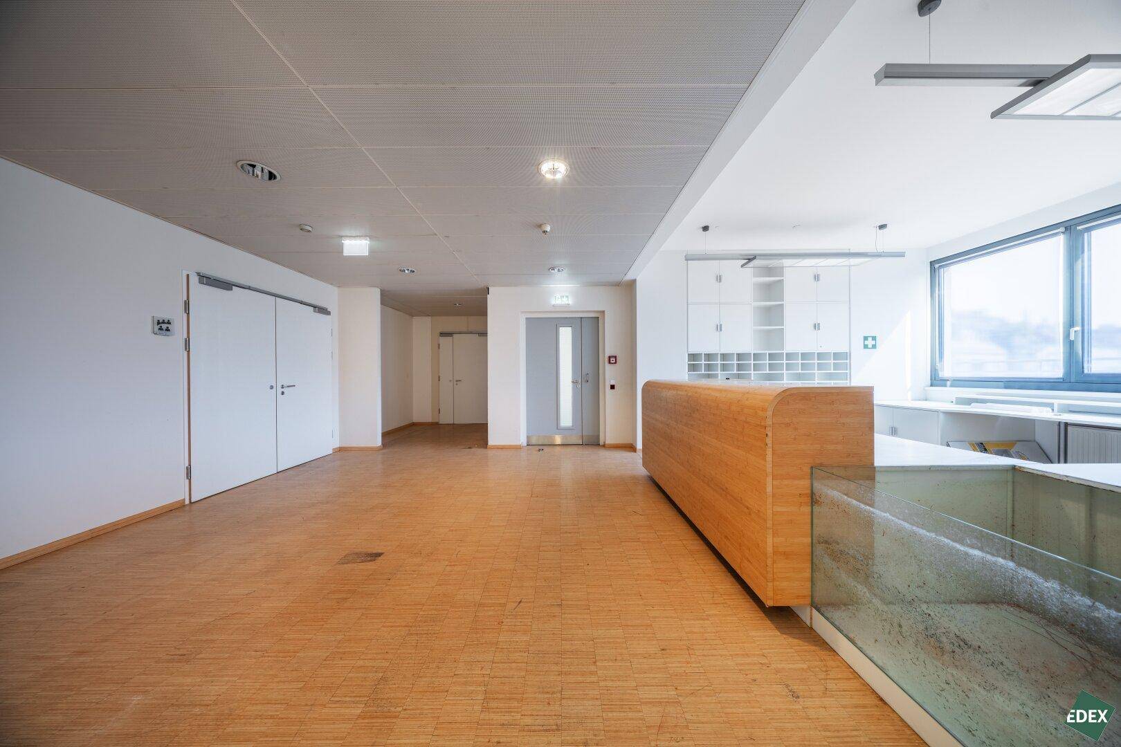 Empfangsbereich mit Holzboden, moderner Theke und Zugang zu einem Aufzug.