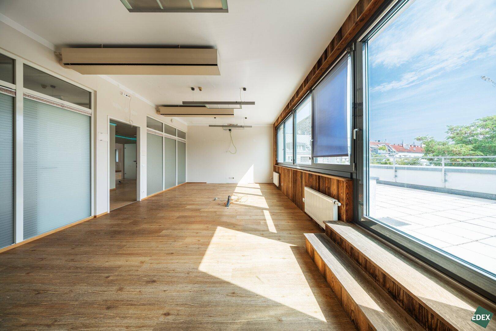 Geräumiger Büroraum mit Holzwandverkleidung, großen Fenstern und Zugang zur Terrasse.