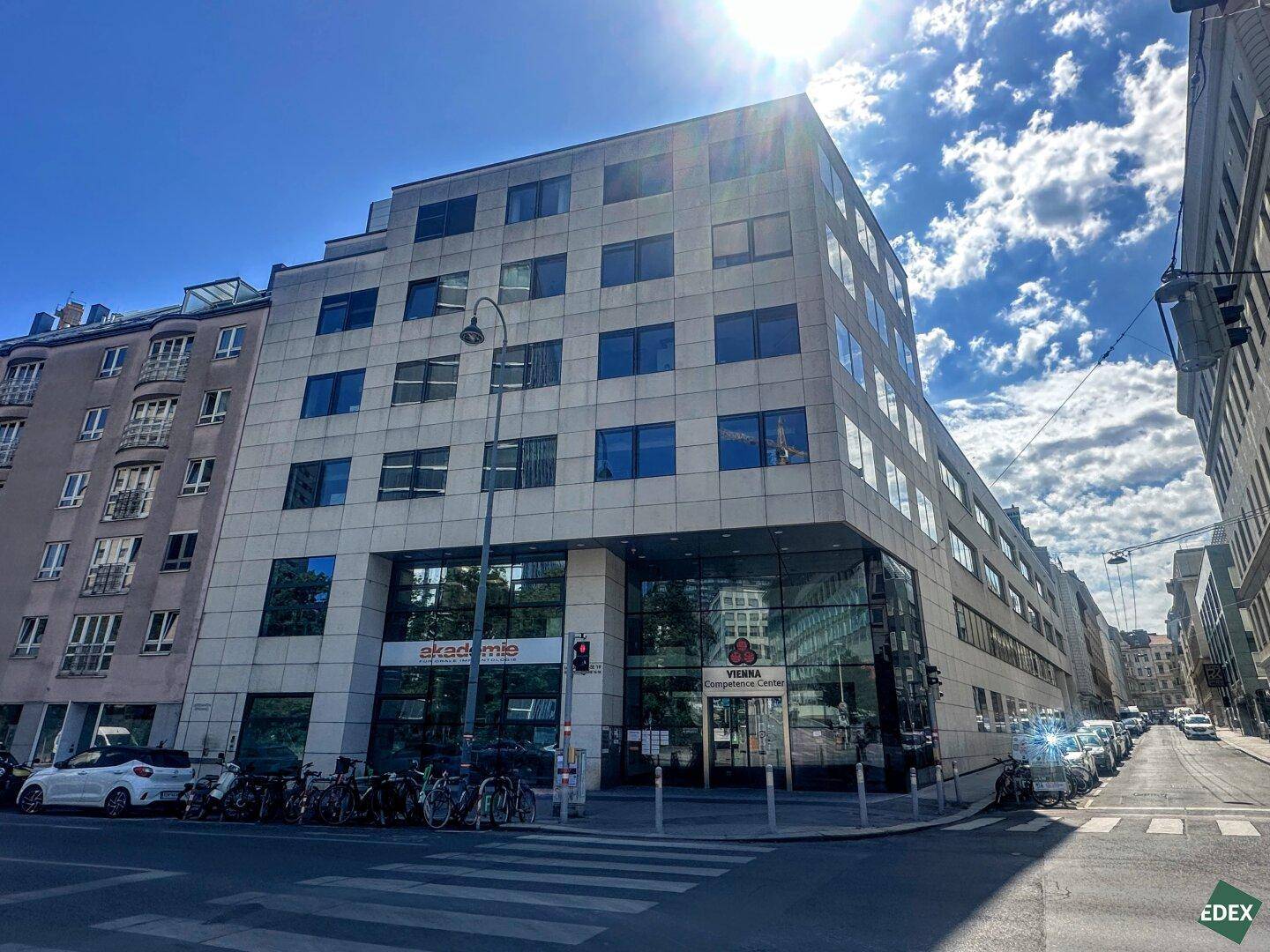 Modernes Bürogebäude an einer belebten Straße mit vielen Fenstern und Geschäften im Erdgeschoss.