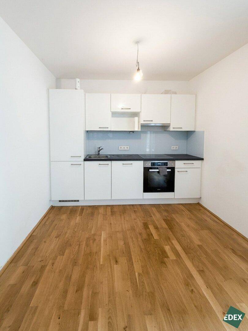 Kompakte Küche mit weißen Schränken, dunkler Arbeitsplatte und Holzboden, bereit zur Nutzung.