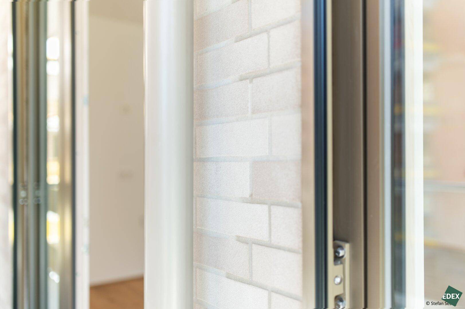 Detailaufnahme eines Fensterrahmens und einer Wand mit dezenter Ziegelstruktur.