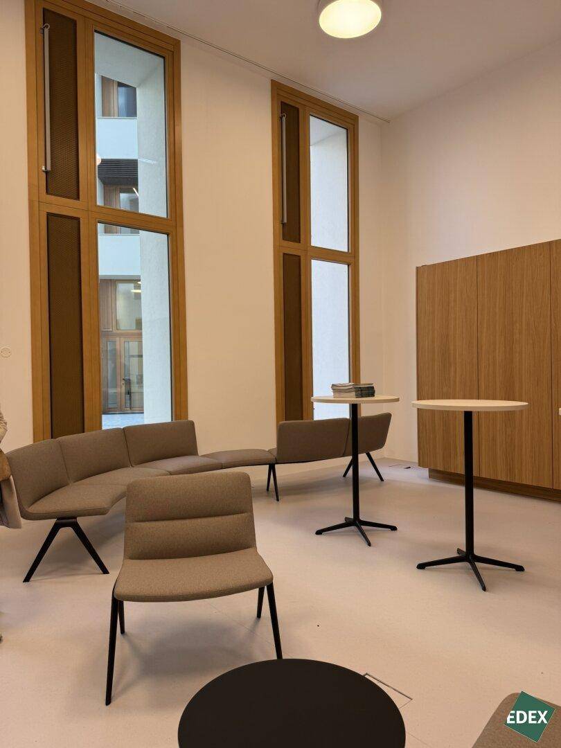 Gemütlicher Loungebereich mit modernen Sitzgelegenheiten und hohen Holzfenstern, ideal für Pausen oder informelle Treffen.