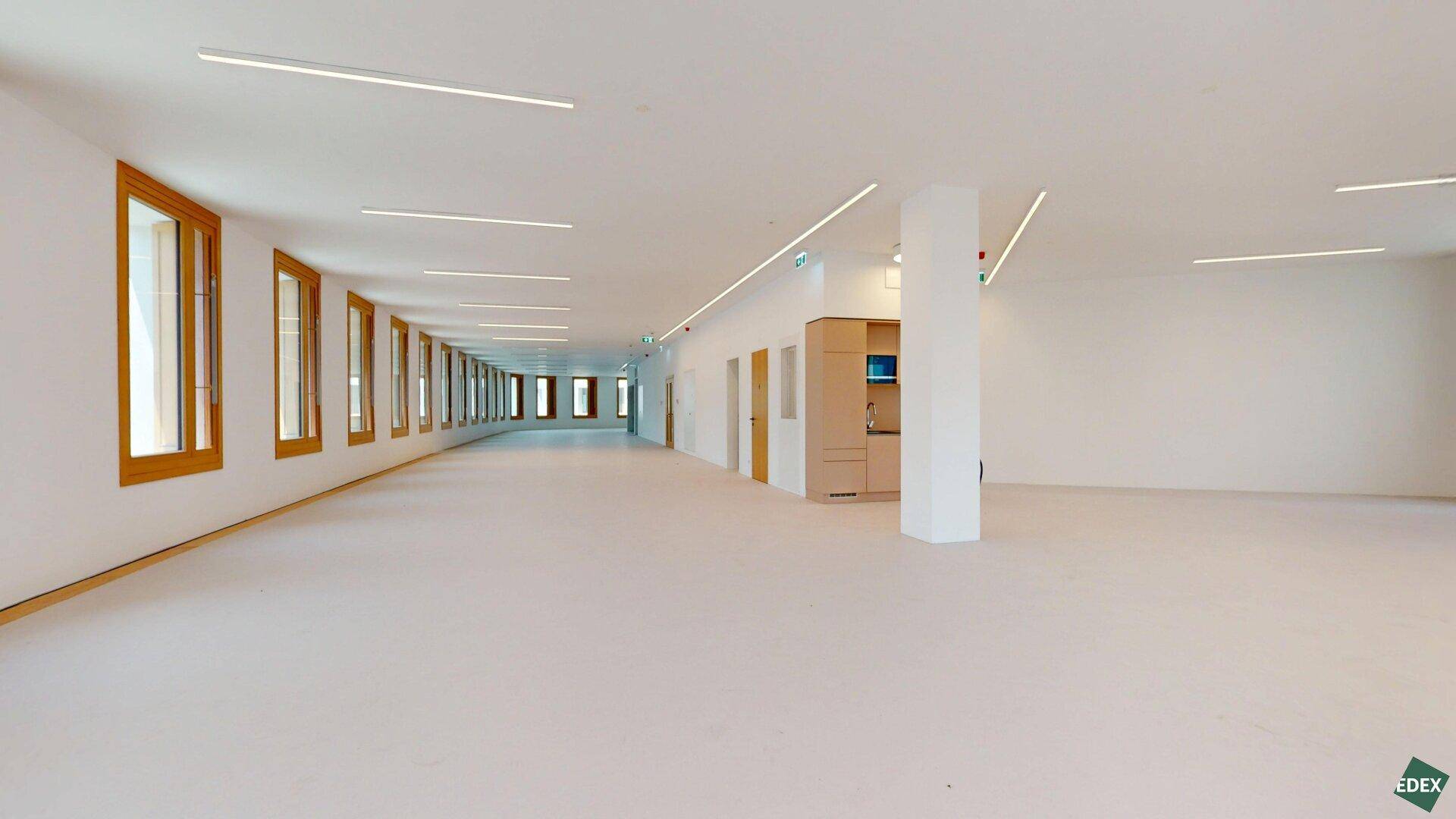 Geräumiger, leerer Bürobereich mit einer Säule und einer kleinen Teeküche im Hintergrund, ideal für flexible Gestaltung.