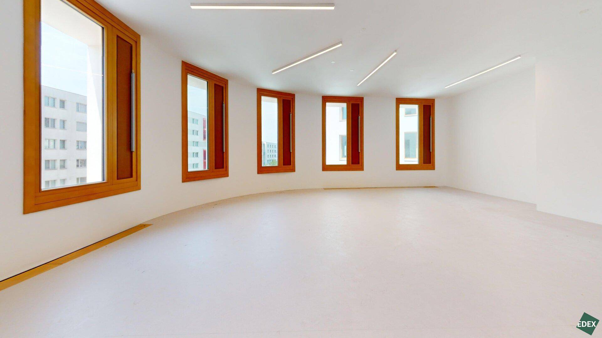 Geschwungener, leerer Büroraum mit mehreren Fenstern und heller Gestaltung, ideal für eine moderne Arbeitsumgebung.