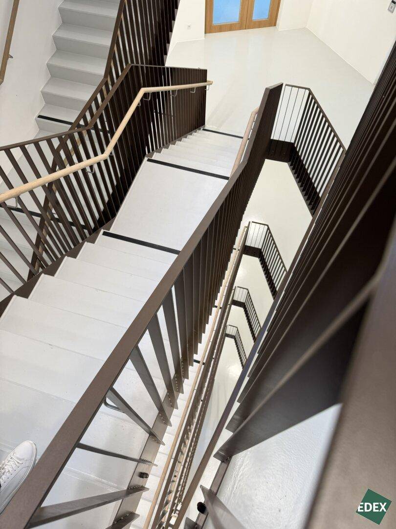 Blick von oben auf ein modernes Treppenhaus mit klaren Linien und robusten Metallgeländern, das sich über mehrere Etagen erstreckt.