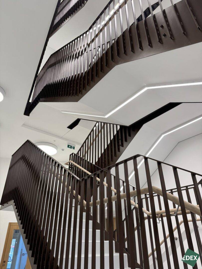 Modernes Treppenhaus mit mehreren Etagen, dunklen Metallgeländern und integrierter Beleuchtung in einem Neubau.