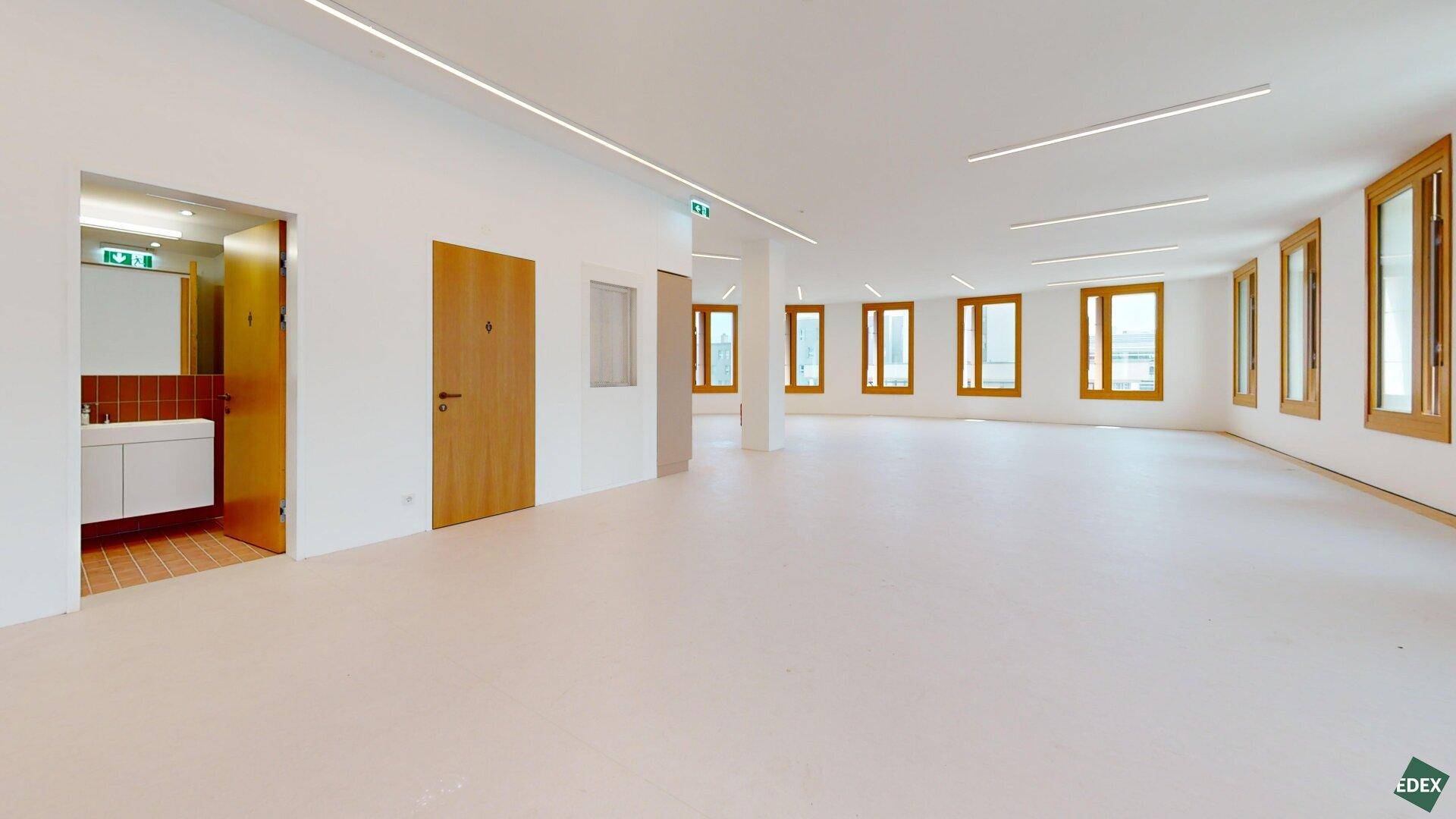 Geräumiger Bürobereich mit Zugang zu einem Badezimmer, vielen Fenstern und moderner Beleuchtung.