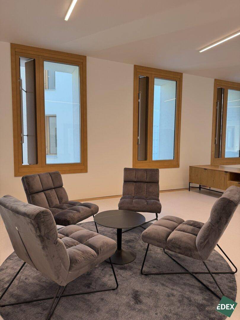 Moderner Loungebereich mit bequemen grauen Sesseln, rundem Teppich und großen Fenstern.