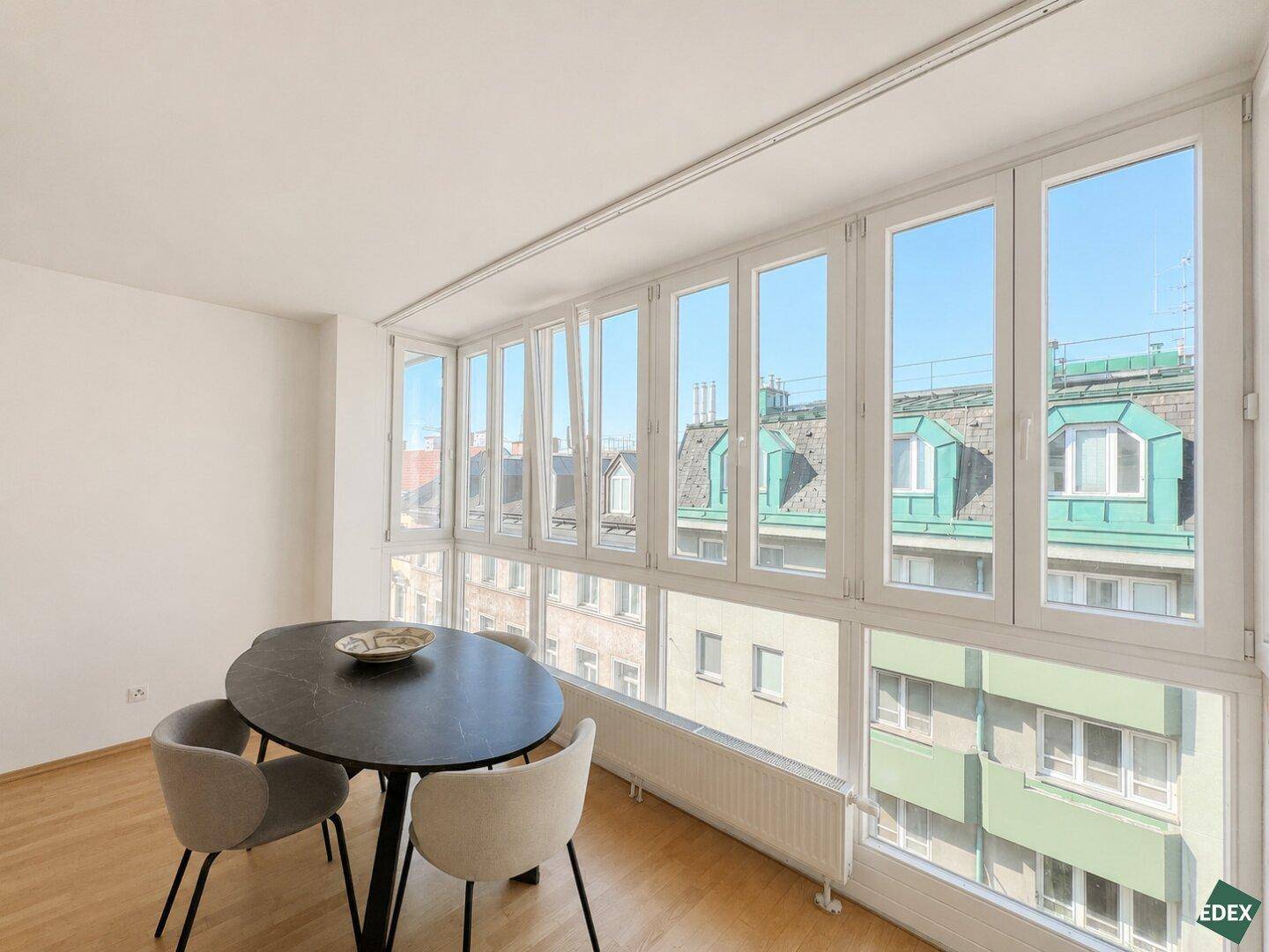 Heller Essbereich mit modernem Tisch und Stühlen, umgeben von großen Fenstern mit Stadtblick.