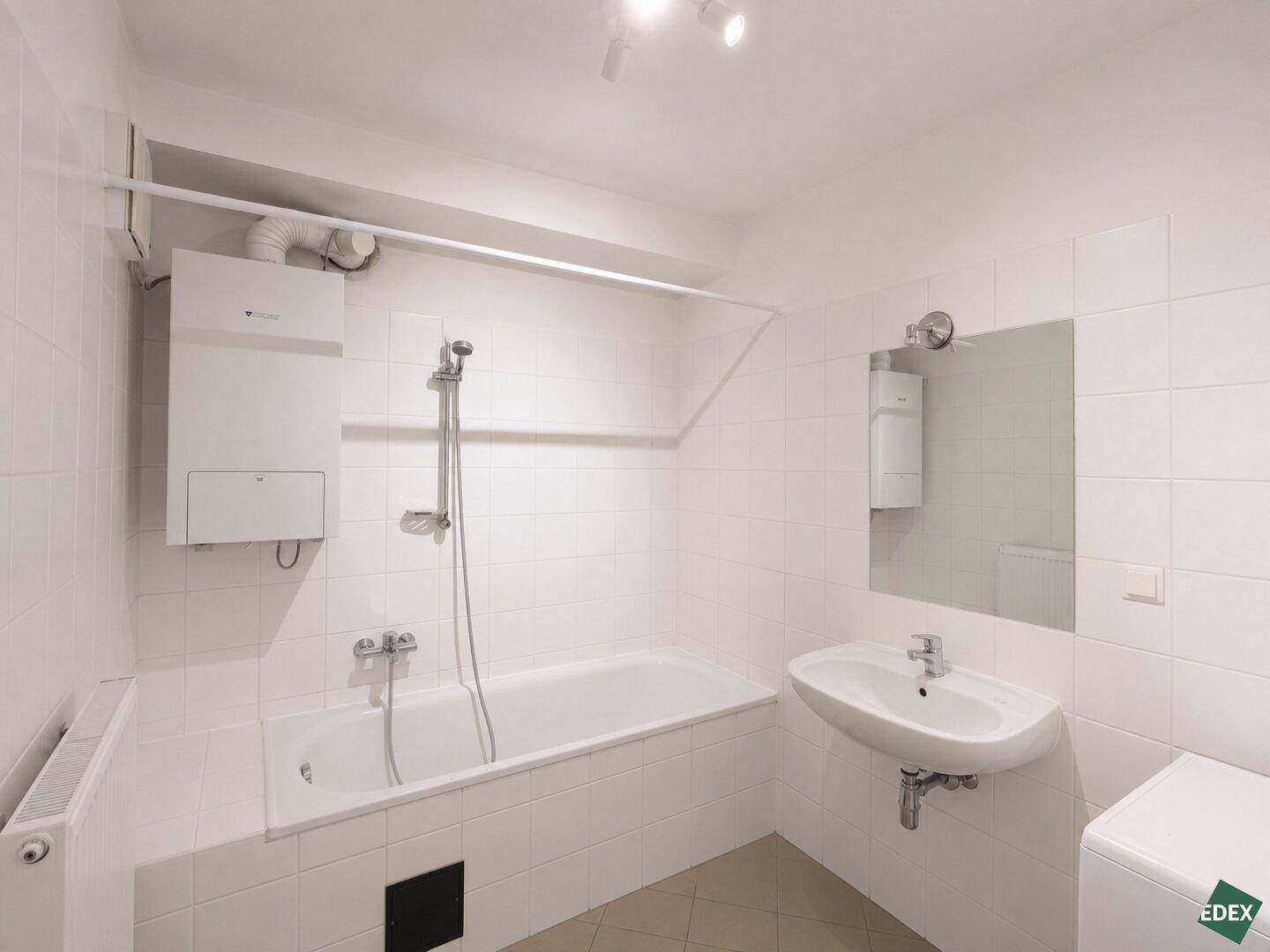 Helles Badezimmer mit Badewanne, Waschbecken und weißen Fliesen an den Wänden.