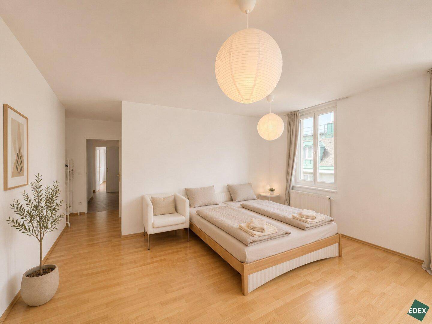 Gemütliches Schlafzimmer mit Holzboden, großem Bett und viel Tageslicht durch das Fenster.