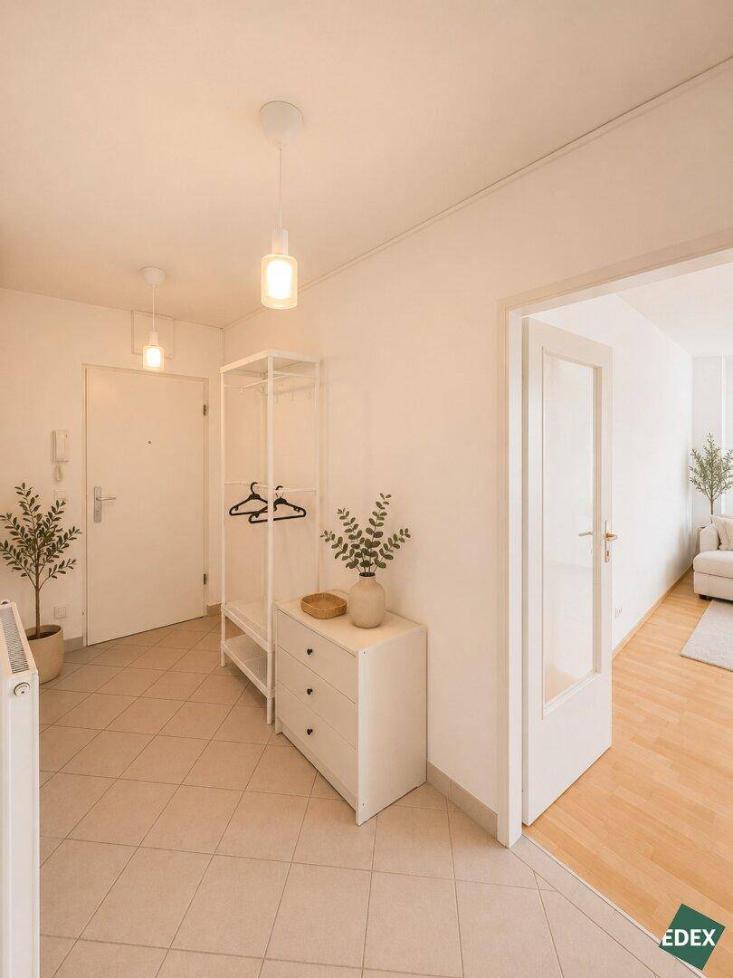 Heller Eingangsbereich mit Fliesenboden, Kommode und Garderobe, führt zu weiteren Räumen.