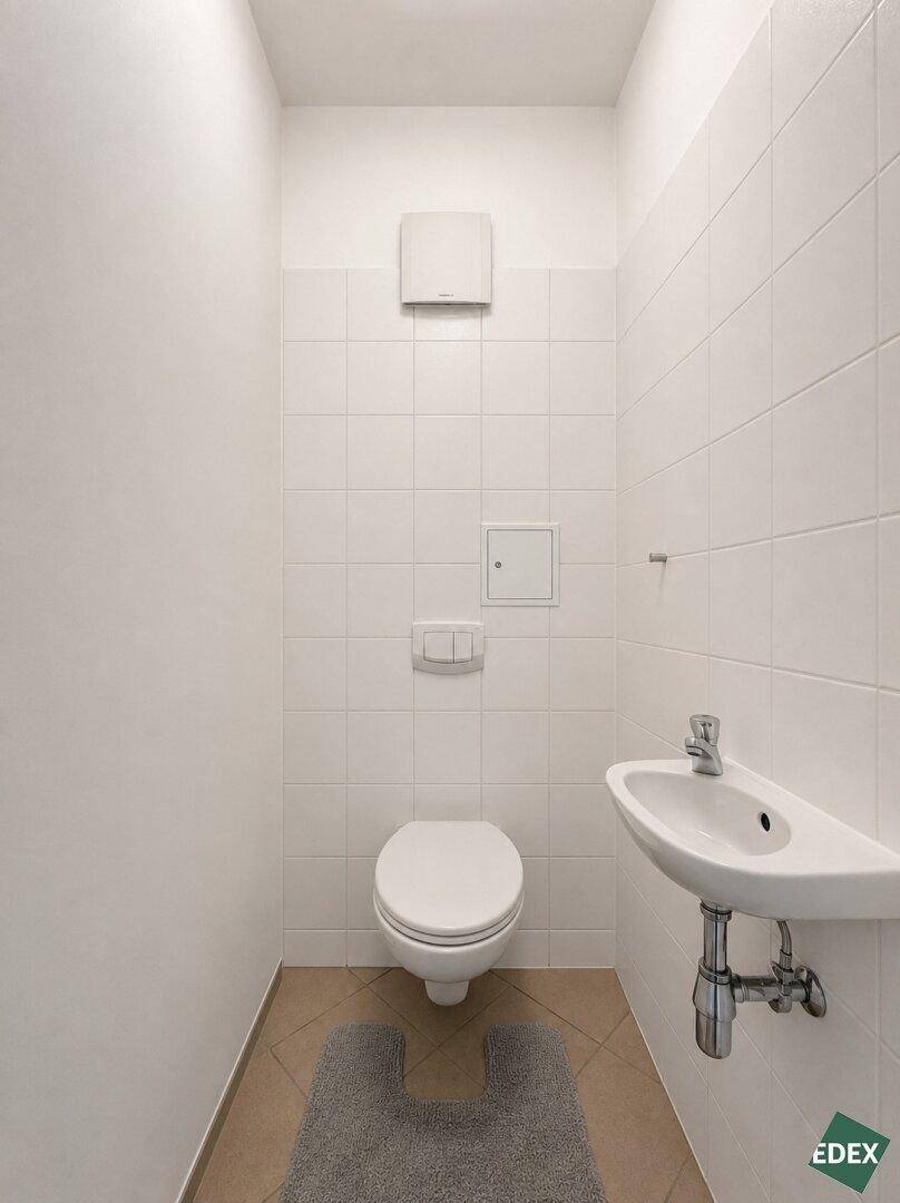 Separates WC mit Toilette, kleinem Waschbecken und weißen Wandfliesen.