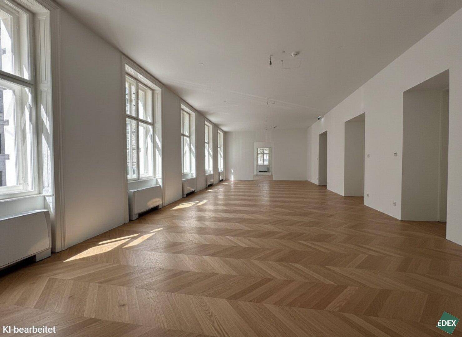Langer, heller Büroraum mit Fischgrätparkett und einer Reihe hoher Fenster, die viel Licht spenden.