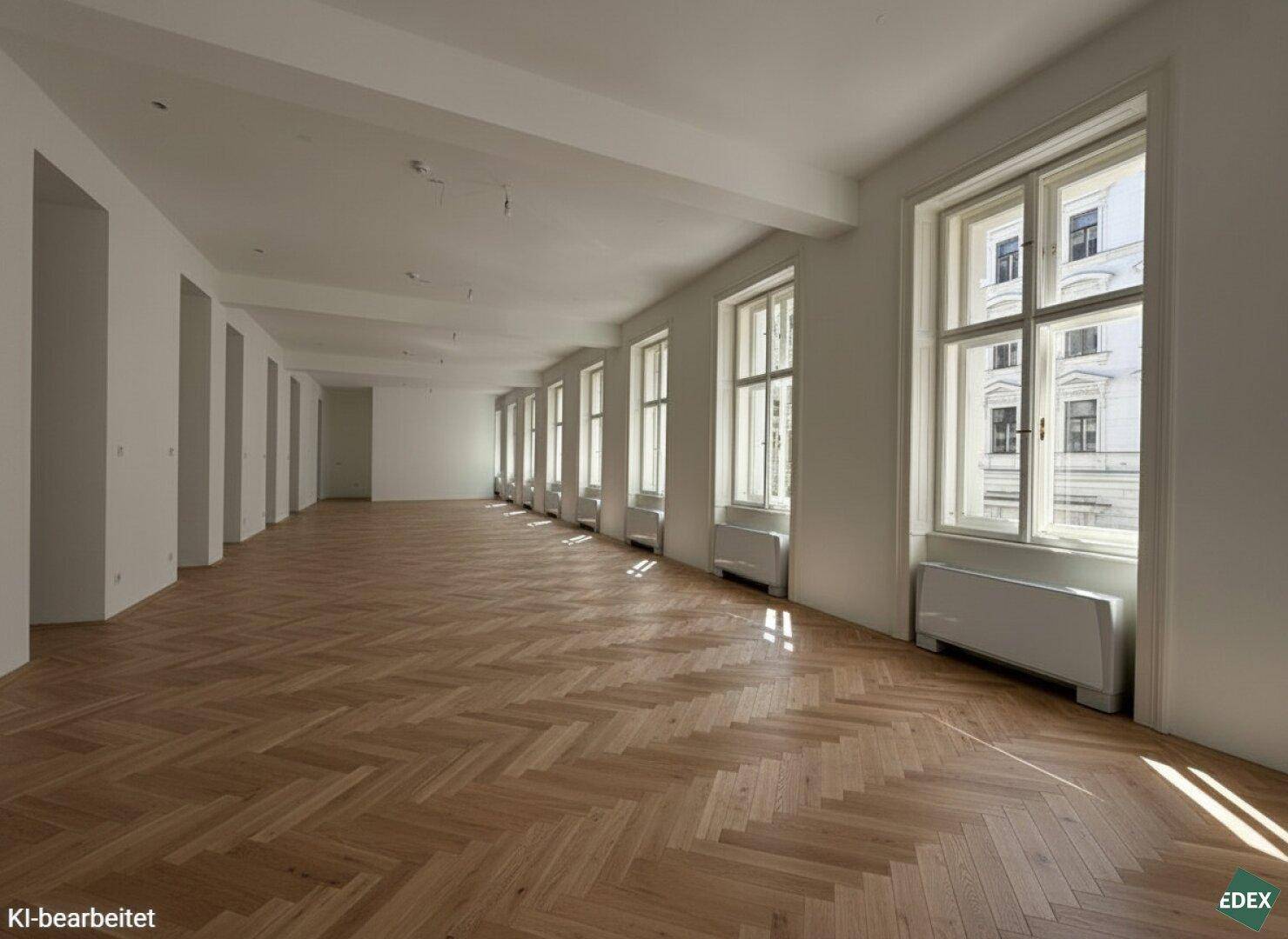 Langer, heller Raum mit Fischgrätparkett und einer Reihe von Fenstern, die den Raum erhellen.