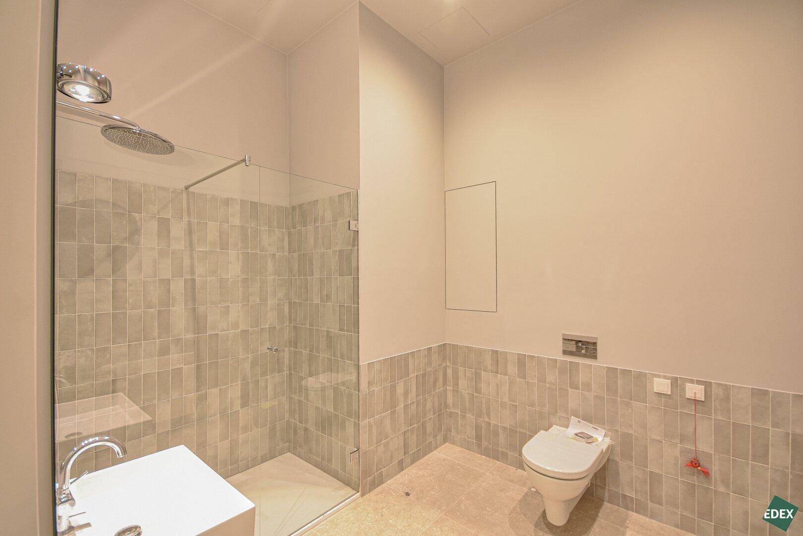 Modernes Badezimmer mit begehbarer Dusche, Wand-WC und grauen Fliesen an Wänden und Boden.
