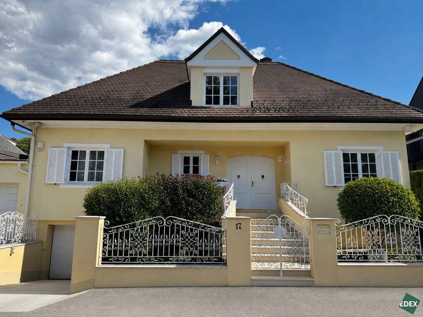 Elegantes gelbes Haus mit weißen Fensterläden, schmiedeeisernem Zaun und klassischem Eingangsbereich.