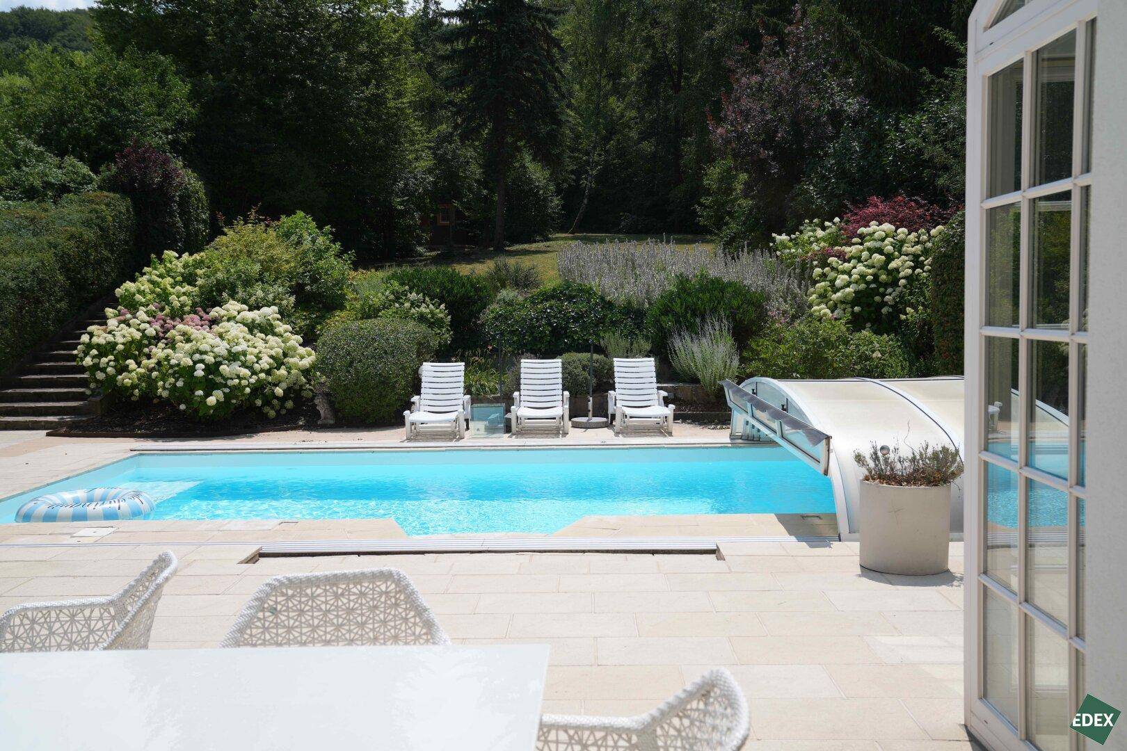 Terrasse mit Swimmingpool, Liegestühlen und üppiger Bepflanzung im Hintergrund.