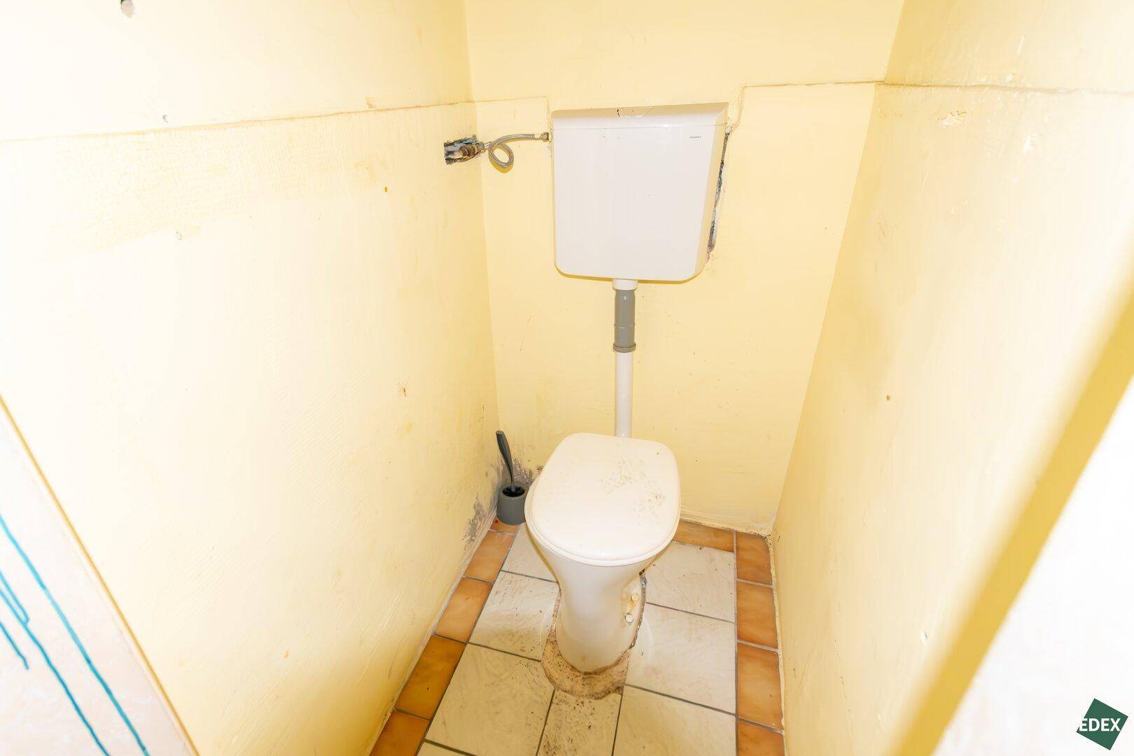 Kleines WC mit Toilette und gelben Wänden, das eine Modernisierung benötigt.
