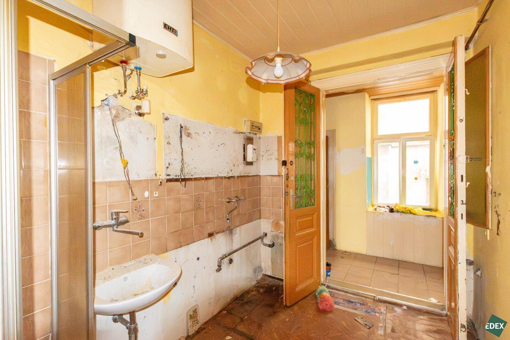 Altes Badezimmer mit Duschkabine, Waschbecken und Fenster, das eine Modernisierung benötigt.