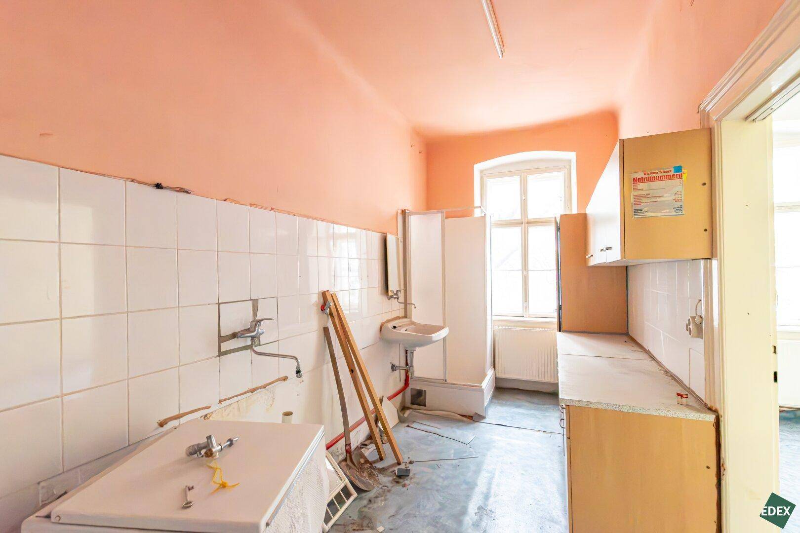 Einfache Küche oder Hauswirtschaftsraum mit rosa Wänden, weißen Fliesen und einem Fenster.