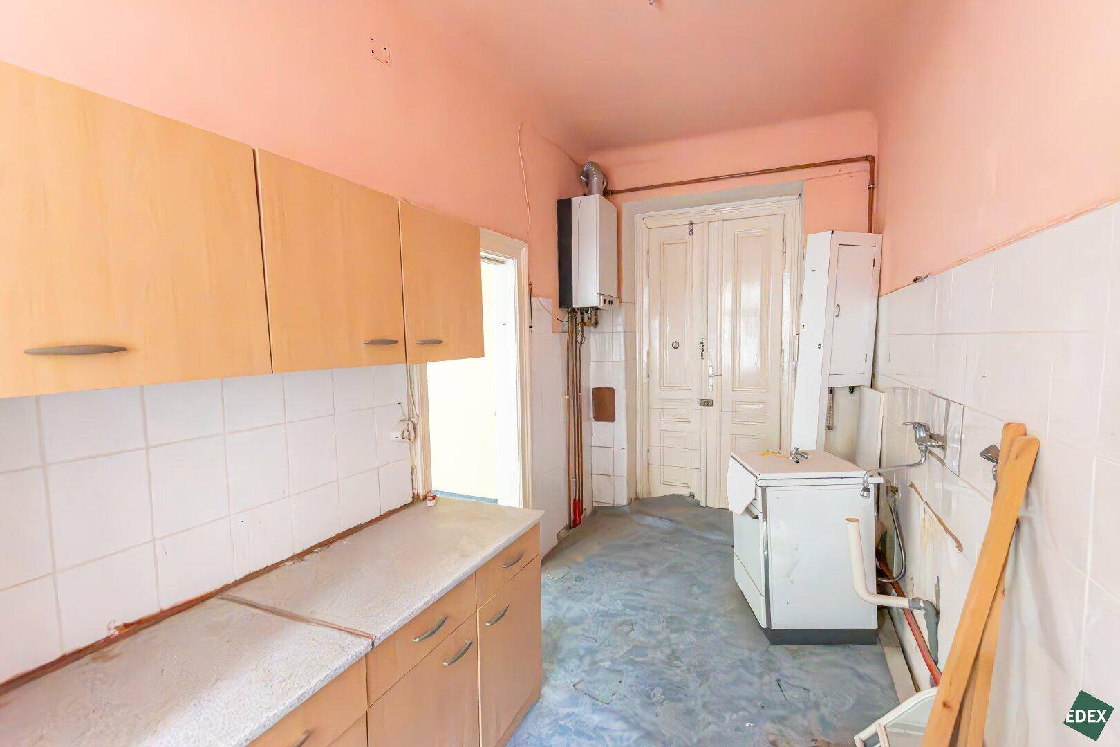 Küche mit einfachen Holzschränken, Gastherme und Doppeltür, die auf Renovierung wartet.