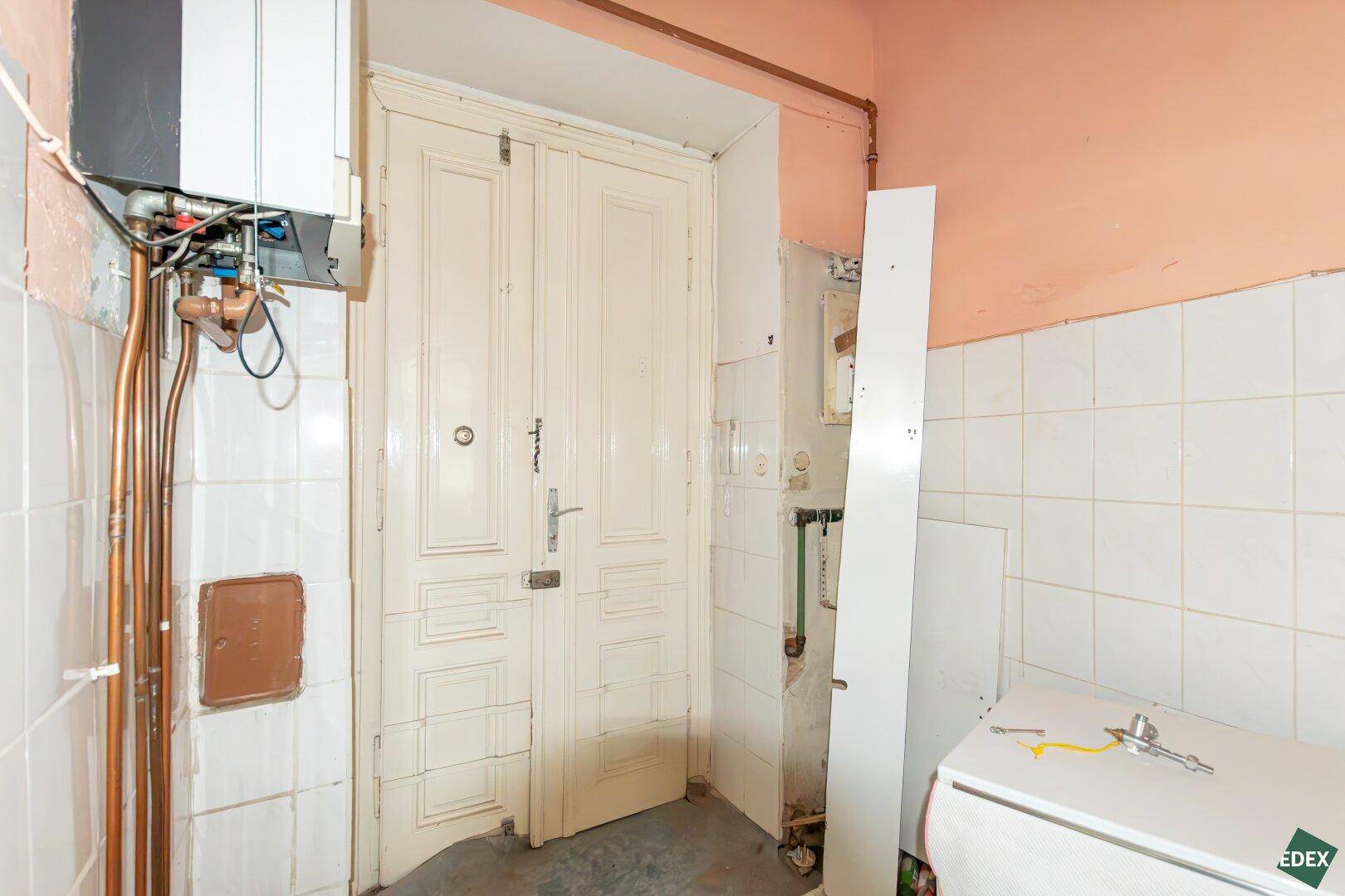 Detailansicht der Doppeltür und des Warmwasserbereiters in einem renovierungsbedürftigen Raum.