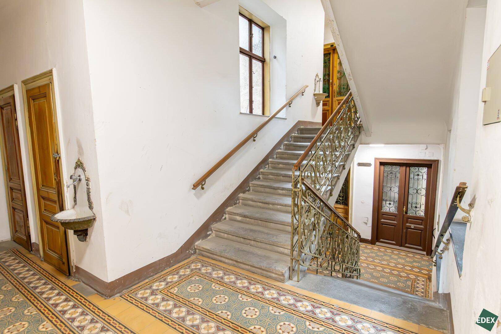 Historisches Treppenhaus mit kunstvollem Geländer und gemusterten Fliesen, das Charme versprüht.