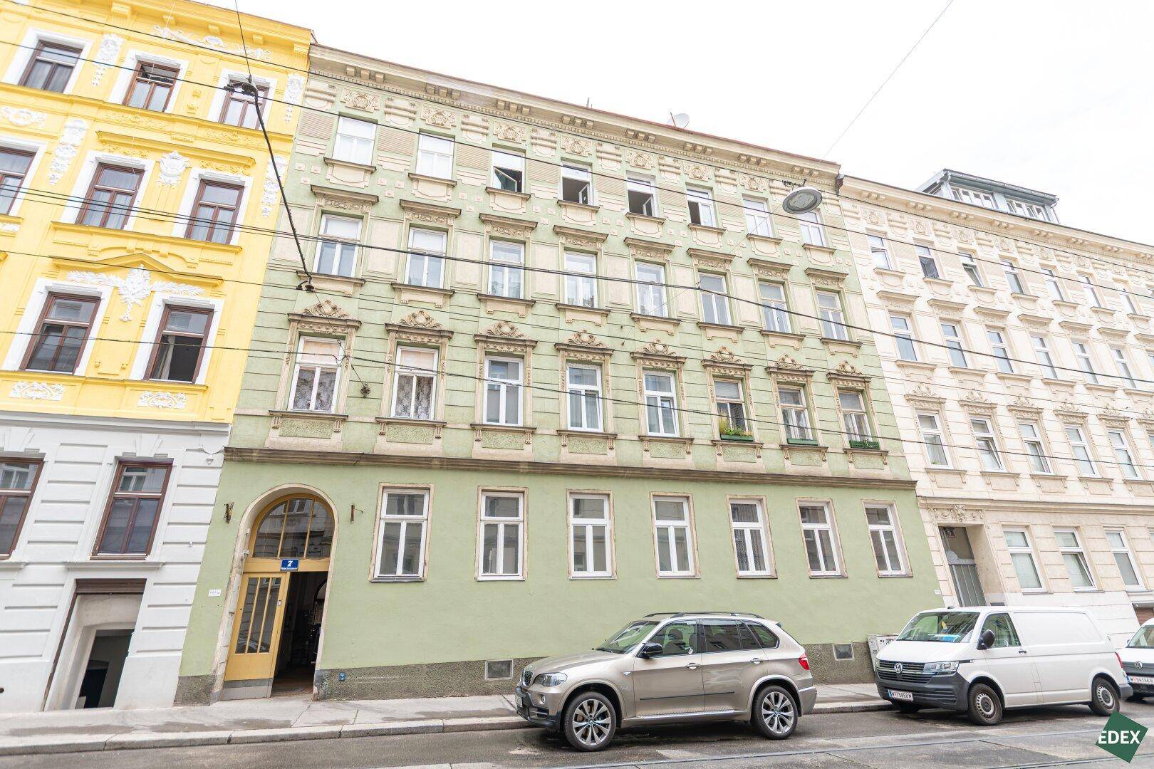 Historische Fassade eines Mehrfamilienhauses an einer Straße mit geparkten Autos.