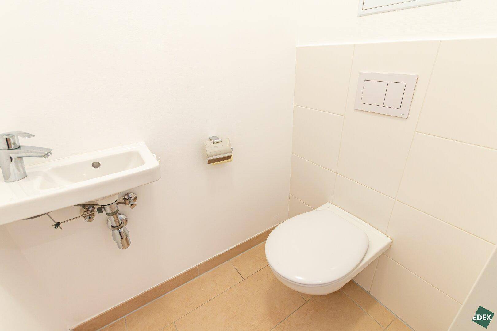 Separates Gäste-WC mit wandhängender Toilette und kleinem Handwaschbecken.