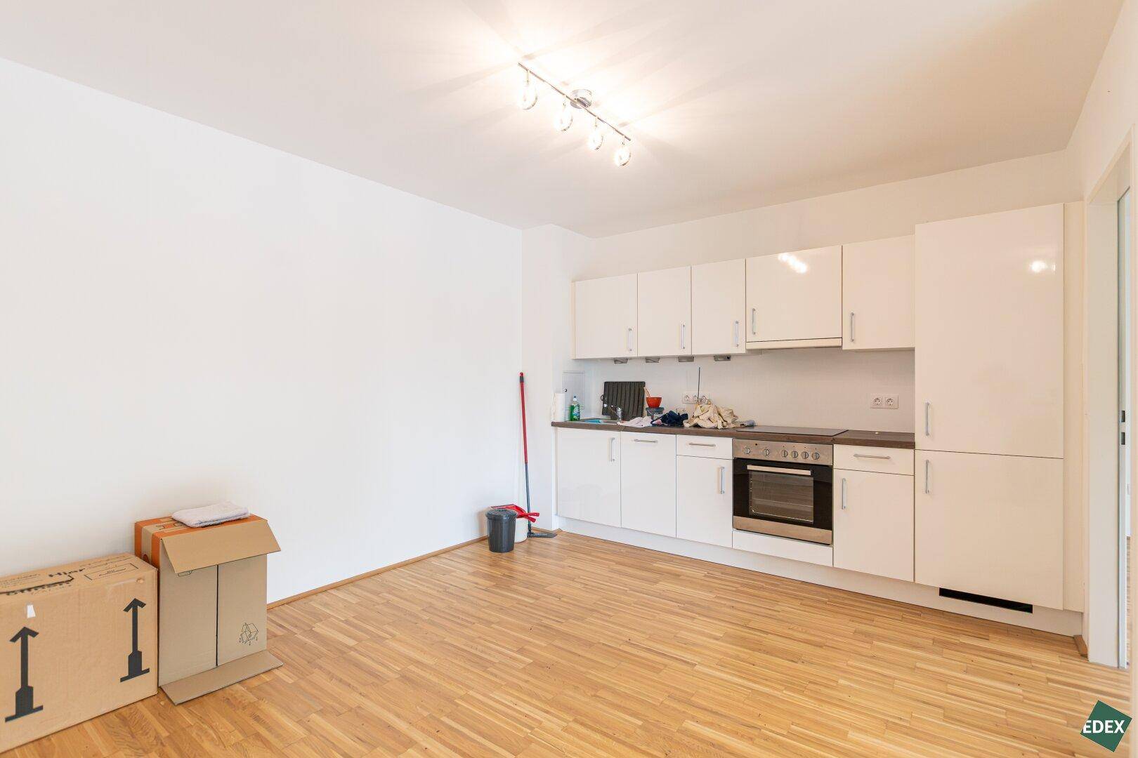Moderne Einbauküche mit weißen Hochglanzfronten und integriertem Backofen in hellem Raum.