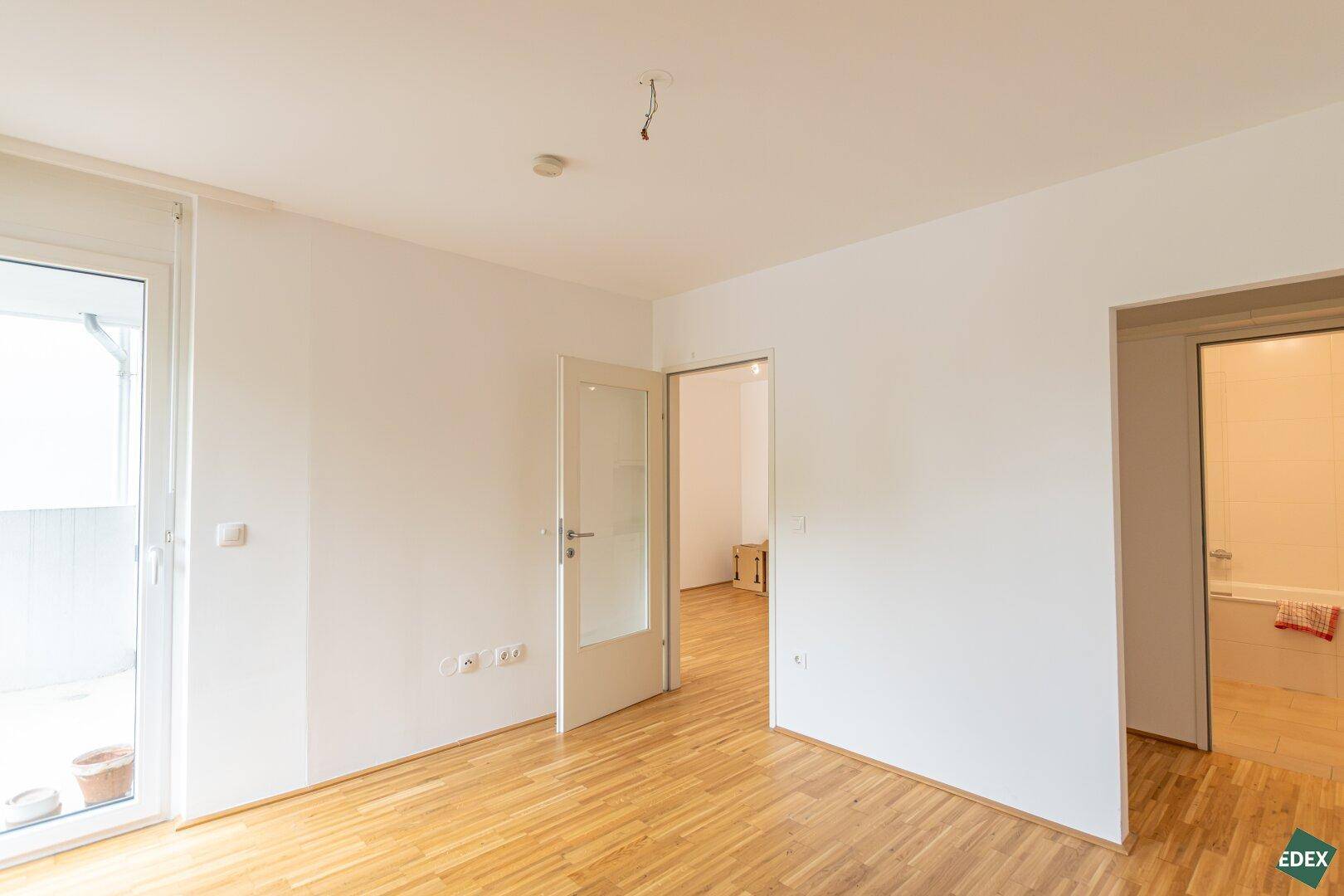 Leeres Zimmer mit Parkettboden und Zugang zu weiteren Räumen, bereit zur individuellen Gestaltung.