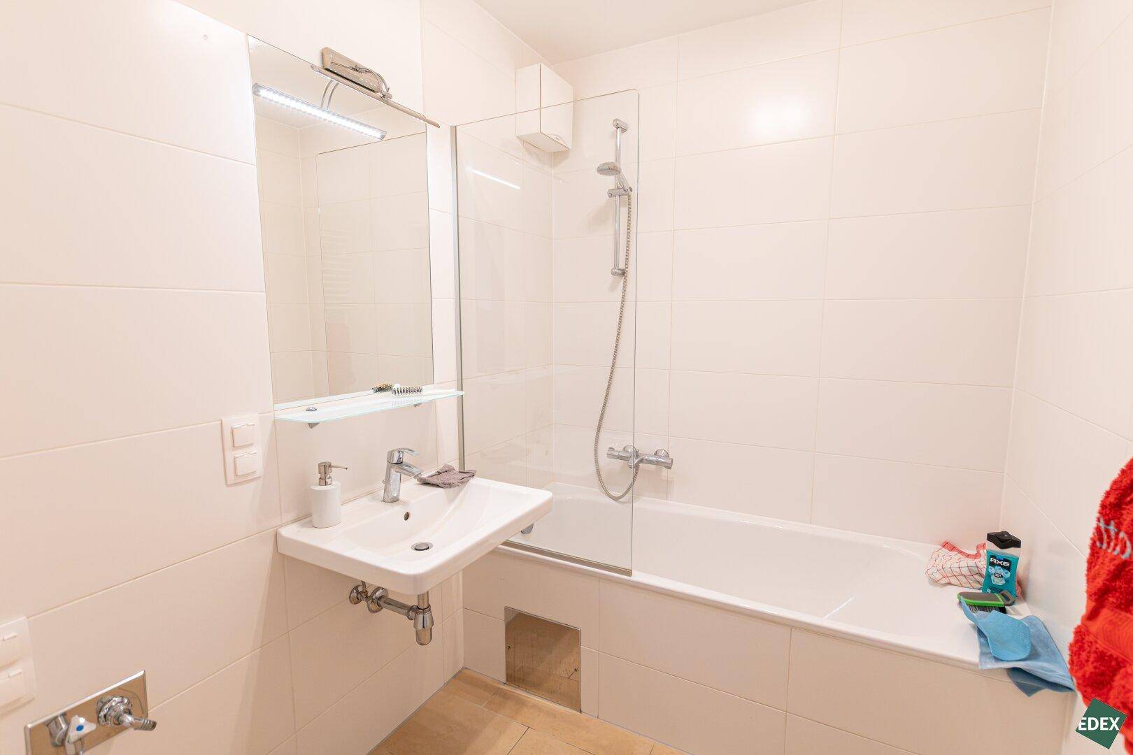 Modern gefliestes Badezimmer mit Badewanne, Duschfunktion und einem einzelnen Waschbecken.