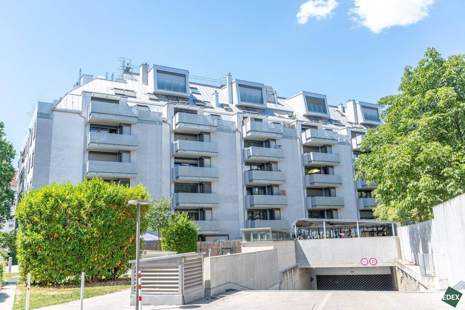 Modernes Mehrfamilienhaus mit Balkonen und Tiefgaragenzufahrt in grüner Umgebung.