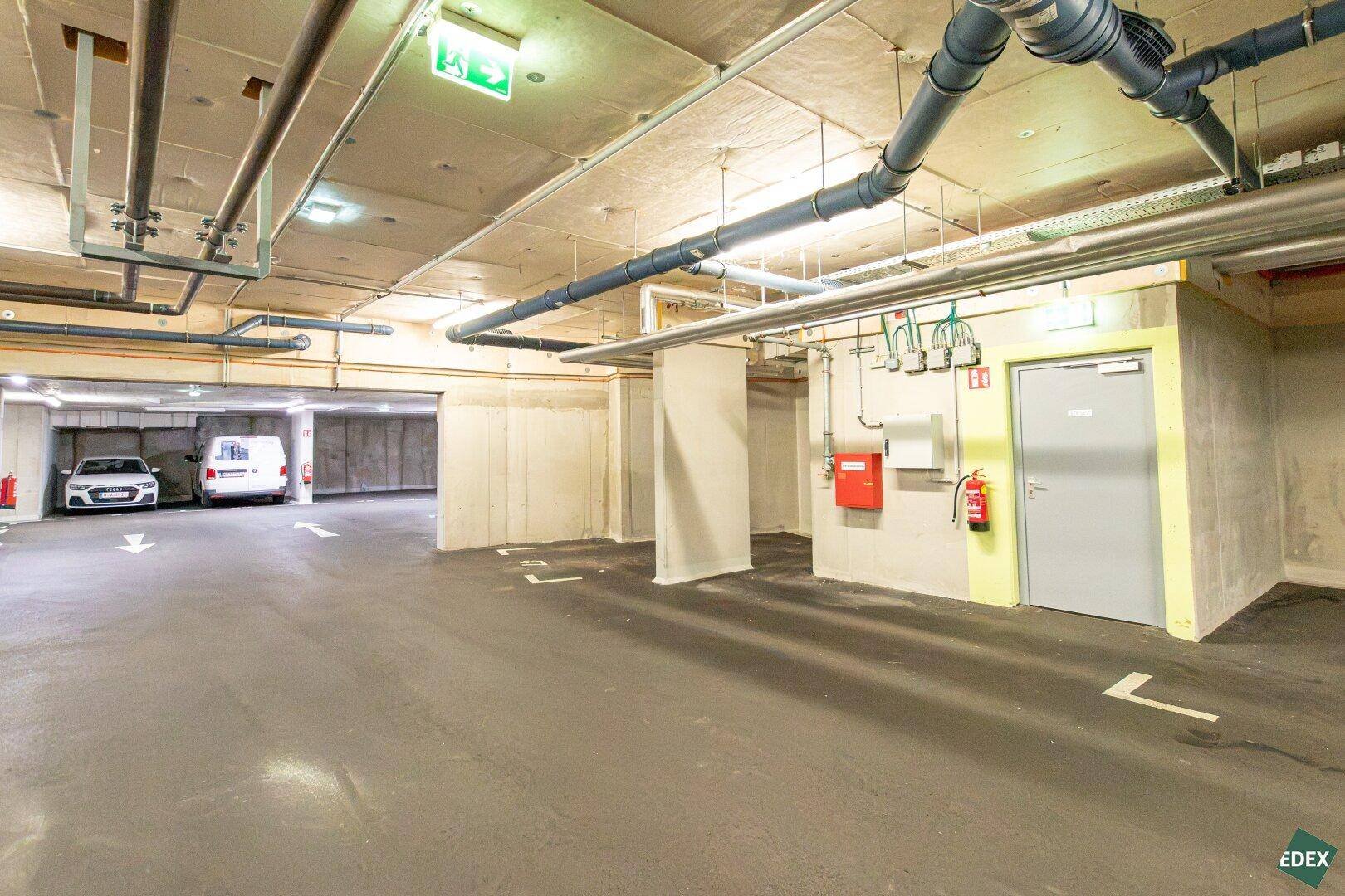 Saubere Tiefgarage mit Betonwänden und sichtbaren Installationen, gut organisiert.
