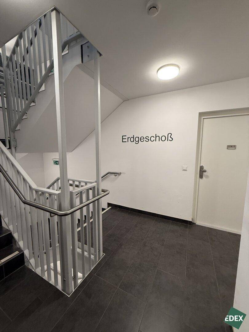 Treppenhaus im Erdgeschoss mit modernem Geländer und Fliesenboden, führt zu den oberen Etagen.