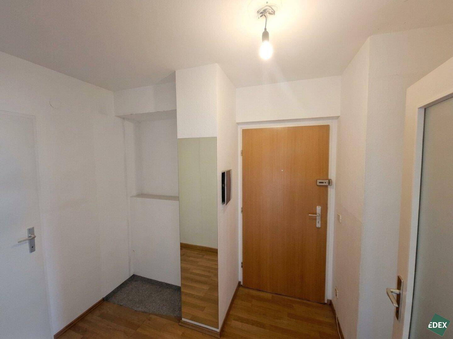 Heller Eingangsbereich mit Holztür und glänzendem Parkettboden, der einladend wirkt.