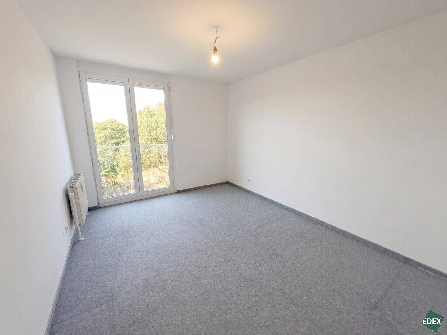 Helles Schlafzimmer mit grauem Teppichboden und Zugang zu einem französischen Balkon.