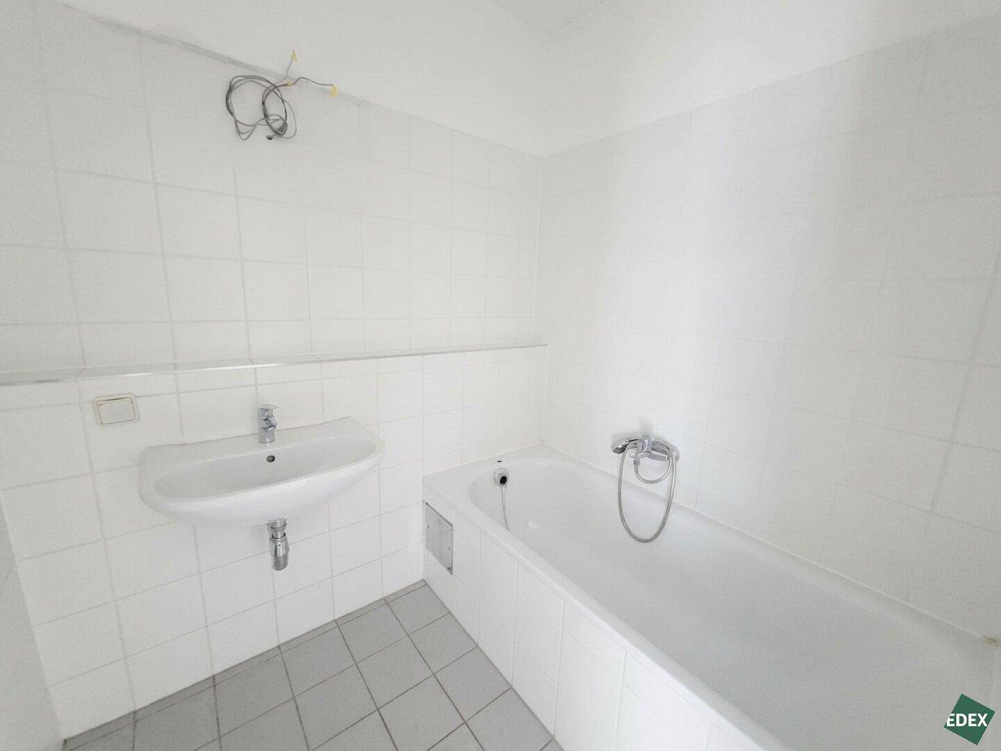 Badezimmer mit weiß gefliesten Wänden, einer Badewanne und einem einzelnen Waschbecken.