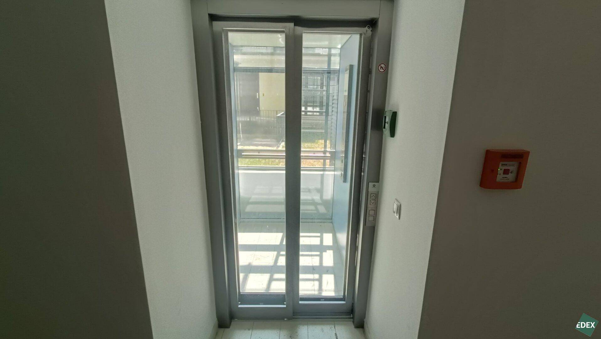 Moderner Glasaufzug im Innenbereich des Gebäudes mit Blick nach draußen.