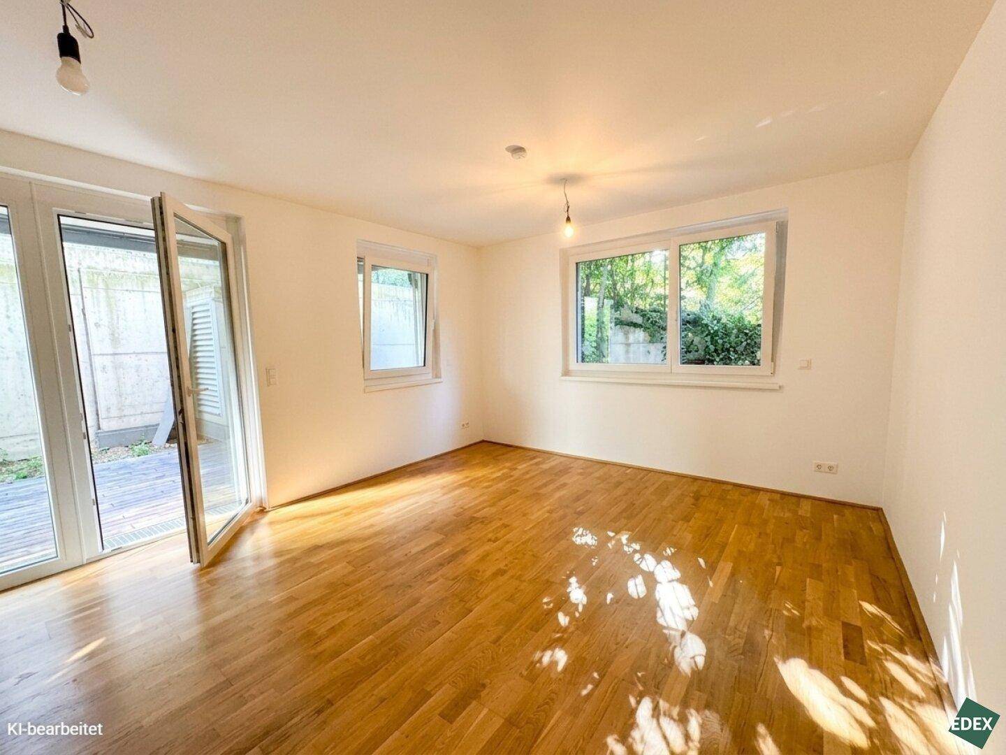Lichtdurchflutetes Zimmer mit Holzboden und großen Fenstern, die viel Tageslicht hereinlassen.