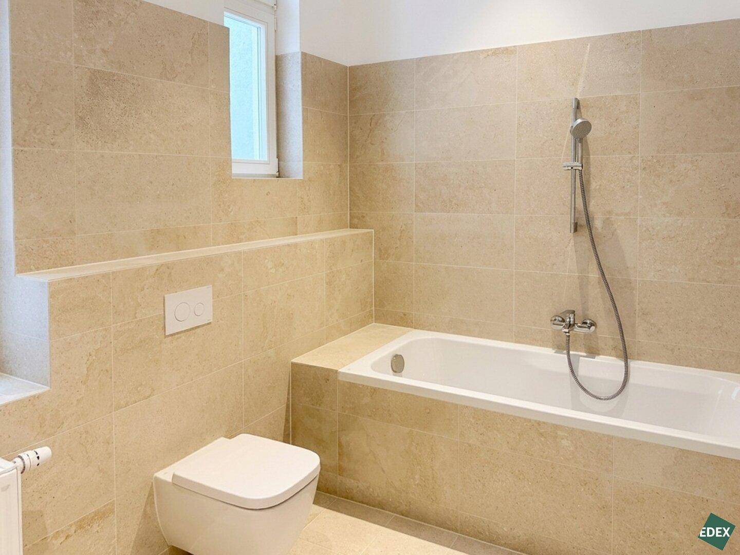 Elegantes Badezimmer mit Badewanne, Wand-WC und beigefarbenen Fliesen, die eine ruhige Atmosphäre schaffen.