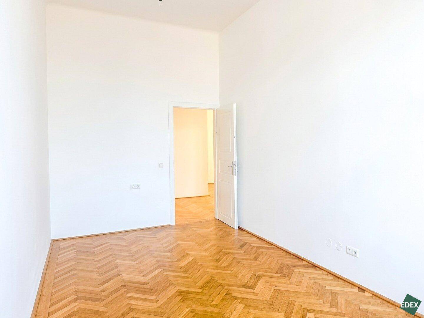 Heller Raum mit Fischgrätparkett und einer Tür, die zu einem weiteren Zimmer führt, ideal als Schlafzimmer.