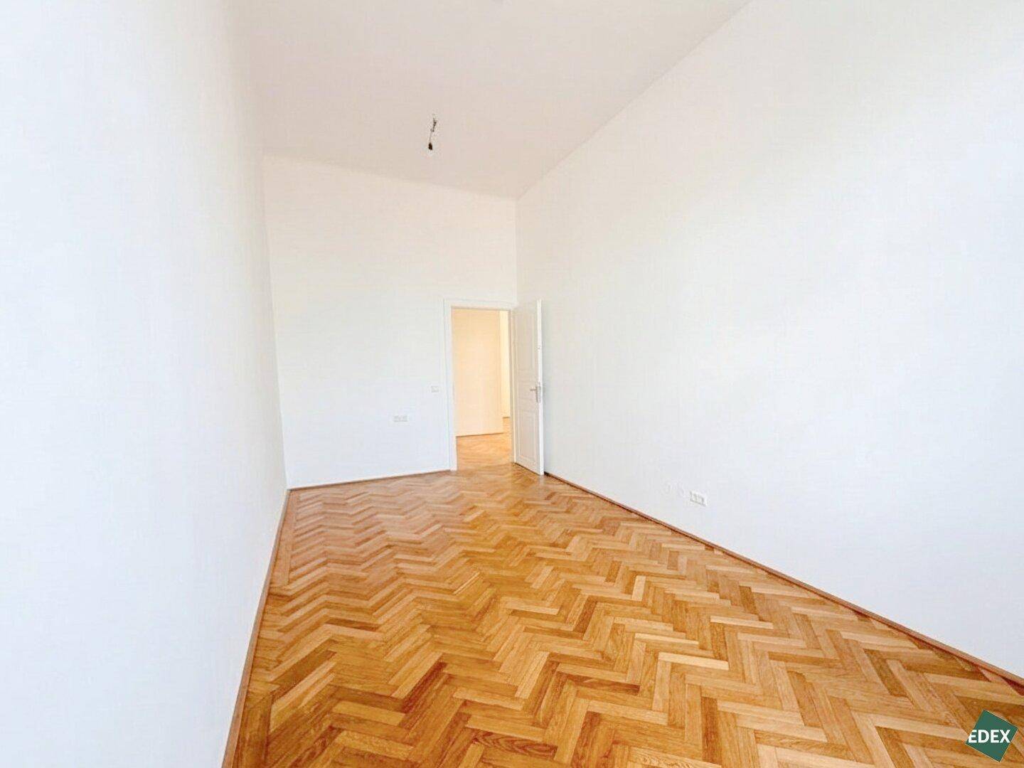 Heller Raum mit Fischgrätparkett und einer Tür, die zu einem weiteren Zimmer führt, ideal als Schlafzimmer.