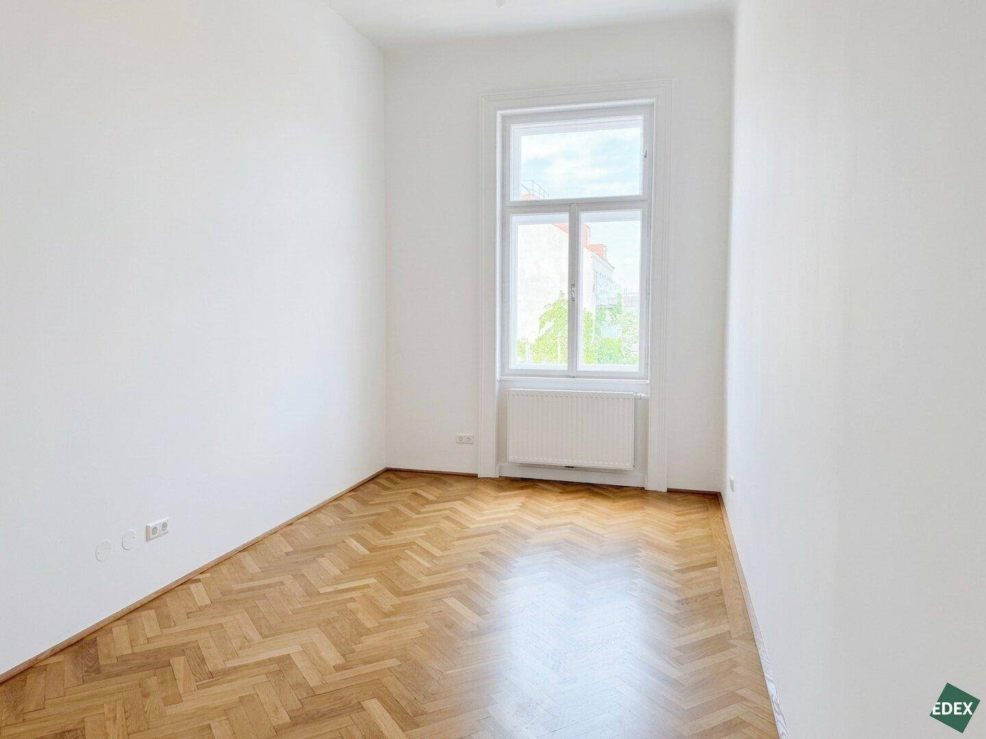 Gemütliches Schlafzimmer mit hellem Fischgrätparkett und einem großen Fenster, das den Raum mit Licht füllt.