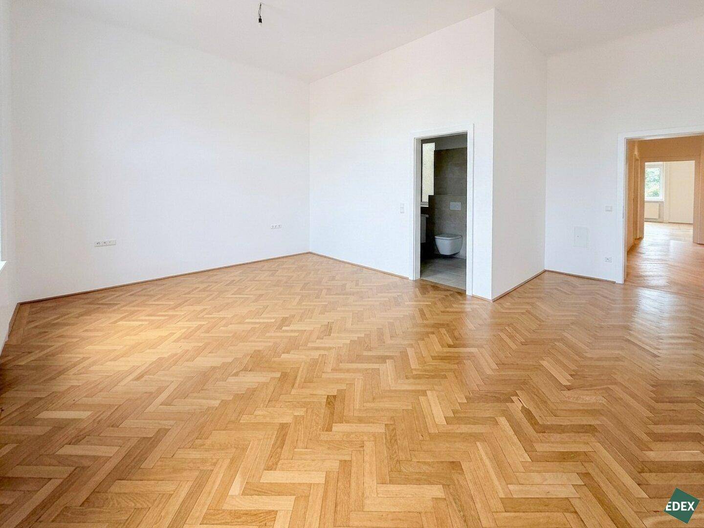 Offener Wohnbereich mit Fischgrätparkett und Zugang zu einem modernen Badezimmer oder Gäste-WC.
